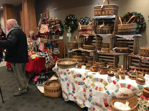A craft fair display featuring various woven baskets, quilts, and holiday decorations in a cozy indoor setting.