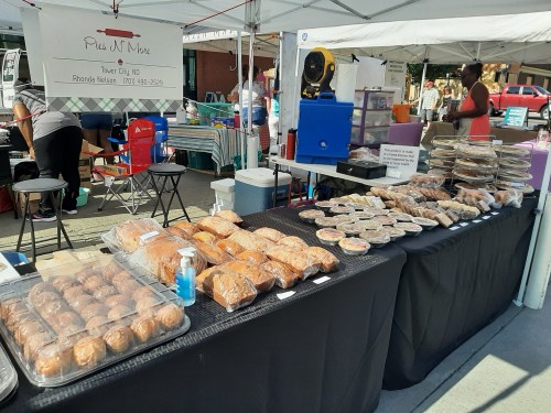 A market stall displaying various baked goods, including muffins and pastries, under a tent.