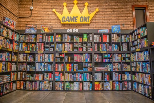 A colorful wall of board games on shelves, with a "GAME ON!" crown sign above.