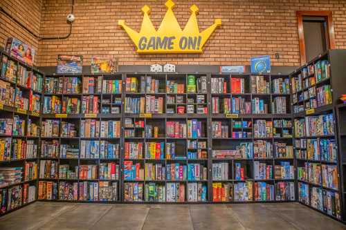 A colorful wall of board games on shelves, with a "GAME ON!" crown sign above.