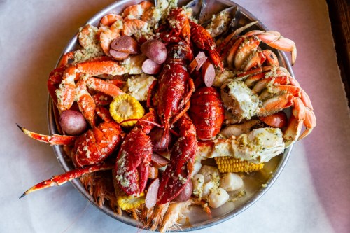 A large platter filled with various seafood, including shrimp, crab, lobster, and corn, garnished with spices.