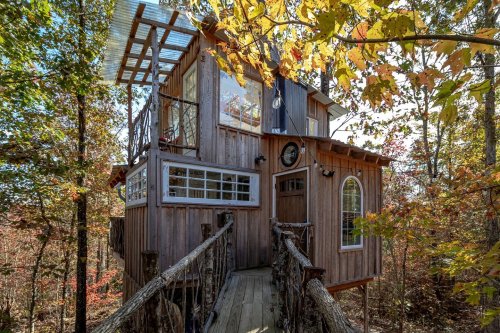 A charming treehouse nestled among colorful autumn trees, featuring wooden walls and a bridge entrance.
