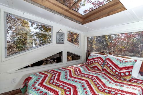 Cozy bedroom with a colorful chevron-patterned quilt and large windows showcasing autumn foliage outside.