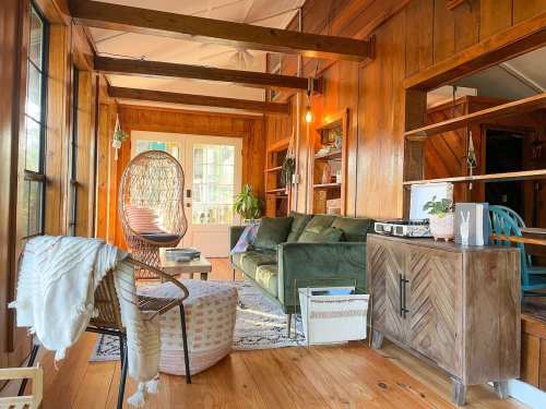 Cozy living space with wooden walls, a green sofa, hanging chair, and warm lighting, creating a welcoming atmosphere.