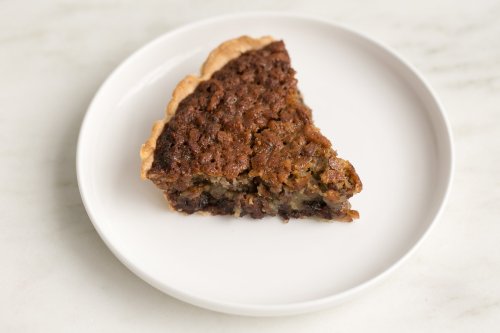 A slice of pie on a white plate, featuring a rich, dark filling and a golden-brown crust.