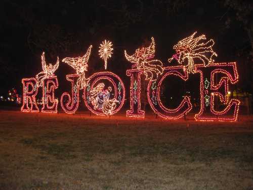 Colorful lights spell out "REJOICE" in a festive display, surrounded by decorative elements in a nighttime setting.