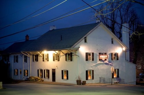 A white building with dark shutters illuminated at night, featuring a sign and surrounded by trees and power lines.