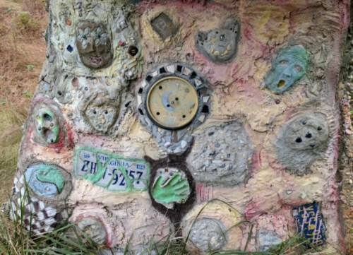 Colorful, textured artwork on a tree trunk featuring faces, shapes, and various decorative elements.