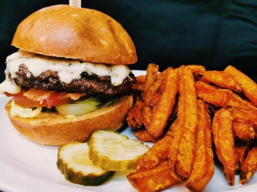 A juicy burger with melted cheese, lettuce, tomato, and pickles, served with crispy sweet potato fries on the side.
