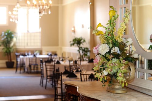 A beautifully arranged floral centerpiece on a table in an elegant dining room with set tables in the background.