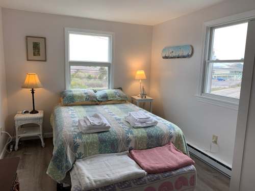 Cozy bedroom with a bed, two windows, a lamp, and neatly arranged towels on a bench. Bright and inviting atmosphere.