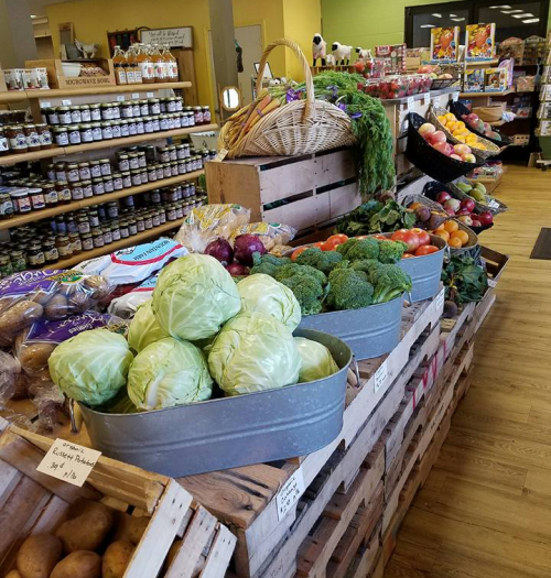 A vibrant display of fresh vegetables and fruits in a market, featuring cabbages, broccoli, and various colorful produce.