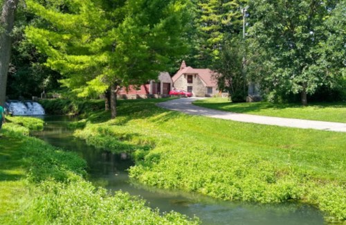 A serene landscape featuring a winding stream, lush greenery, and a quaint house surrounded by trees.