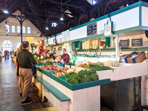 A bustling market stall filled with fresh vegetables, with customers interacting with vendors in a vibrant setting.