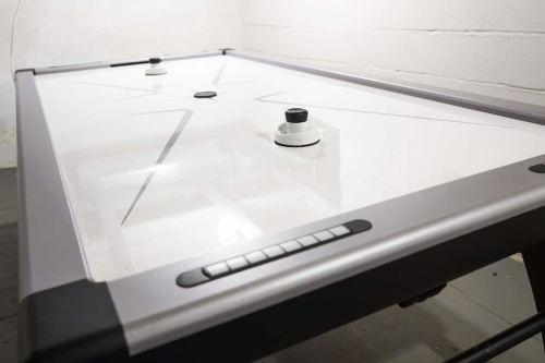 A close-up of a modern air hockey table with a sleek design and two pucks on a white playing surface.