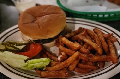 A plate with a hamburger, lettuce, tomato, pickles, and a side of crispy fries.