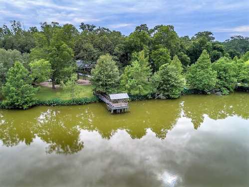 A serene lake surrounded by lush green trees, featuring a small dock reflecting in the calm water.