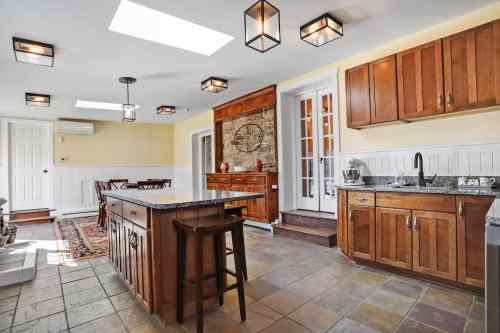Bright kitchen with wooden cabinets, a central island, and large windows, featuring a cozy dining area and stone accents.