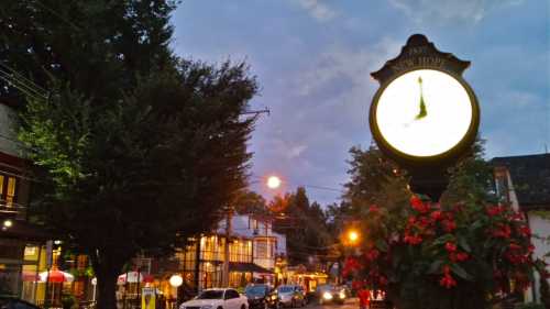 A street scene at dusk featuring a vintage clock, trees, and buildings with warm lights illuminating the area.