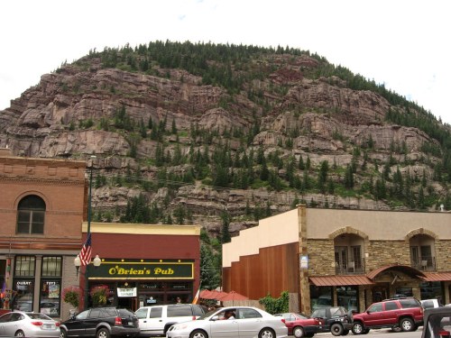 A scenic view of a mountain with trees, overlooking a street with shops and a pub in a small town.