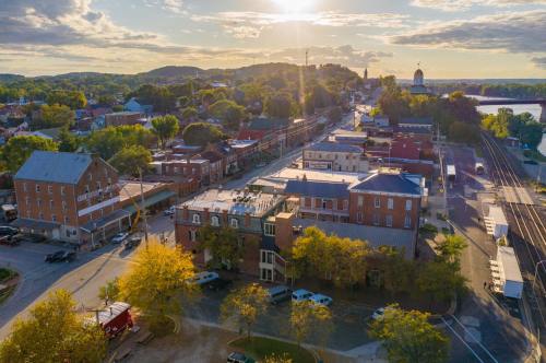 Aerial view of a small town with historic buildings, trees, and a sunset over rolling hills in the background.