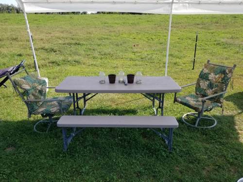 A picnic table with two chairs under a canopy, set on green grass, with small pots and glasses on the table.