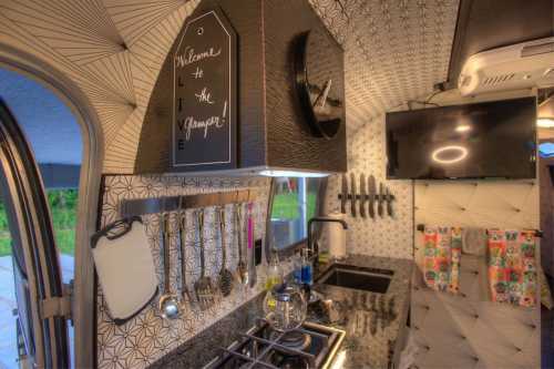 A stylish kitchen in a camper van featuring modern appliances, utensils, and decorative wall patterns.