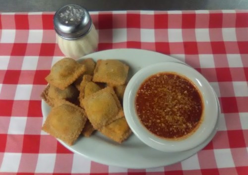 A plate of golden-brown ravioli with marinara sauce and grated cheese, set on a red and white checkered tablecloth.