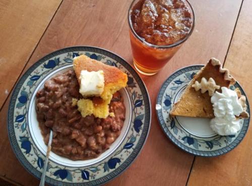 A plate with beans and cornbread, alongside a slice of pie with whipped cream and a glass of iced tea.