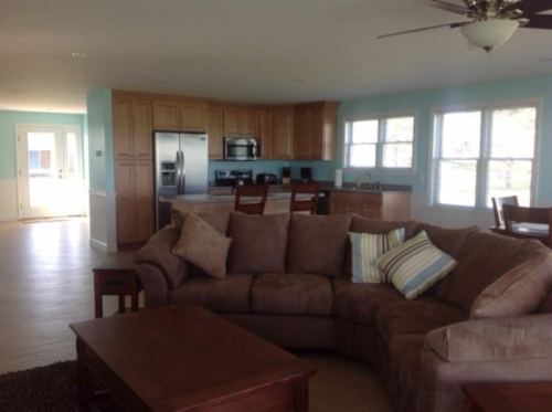 Cozy living room with a large sectional sofa, wooden coffee table, and a kitchen in the background. Bright and airy space.