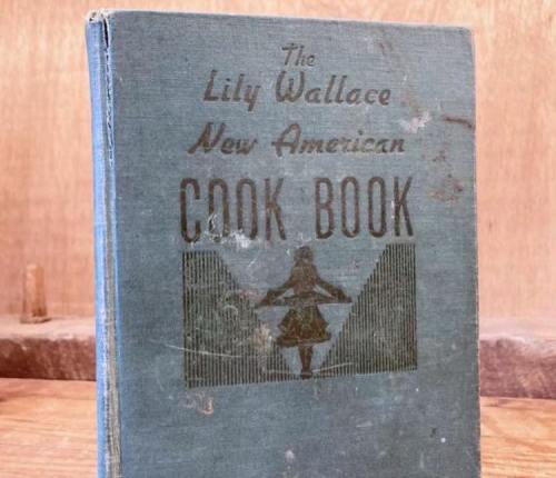 A vintage cookbook titled "The Lily Wallace New American Cook Book" with a worn blue cover.