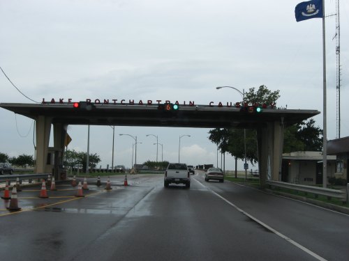 A vehicle approaches the Lake Pontchartrain Causeway toll plaza with traffic lights and construction cones visible.