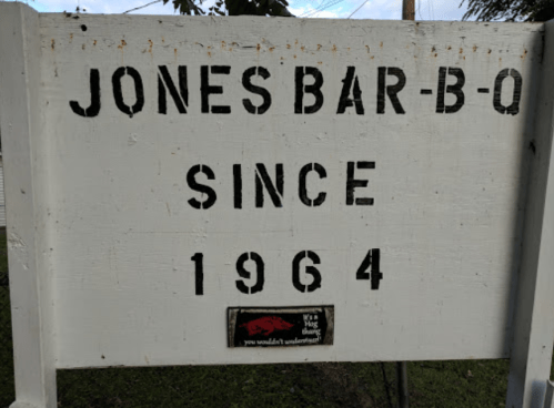 Sign for Jones Bar-B-Q, established in 1964, with a rustic white background and bold black lettering.