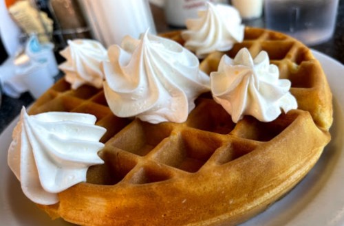 A golden waffle topped with swirls of whipped cream, served on a white plate.