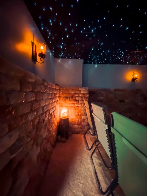 A serene room with salt brick walls, glowing lanterns, and a starry ceiling, featuring comfortable chairs for relaxation.