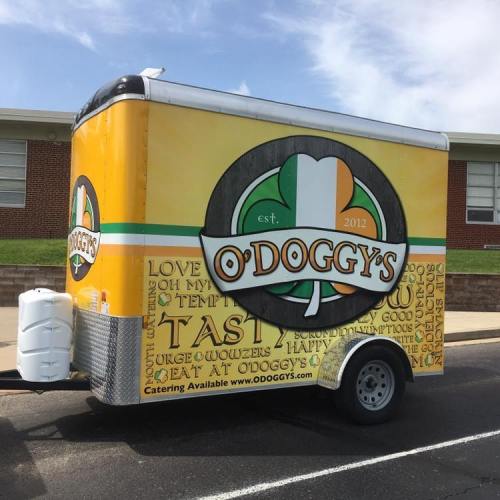 A colorful food trailer with the name "O'Doggy's" and a logo featuring a green, white, and orange design.