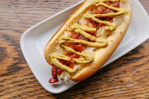 A hot dog topped with sauerkraut and mustard, served on a white plate against a wooden background.