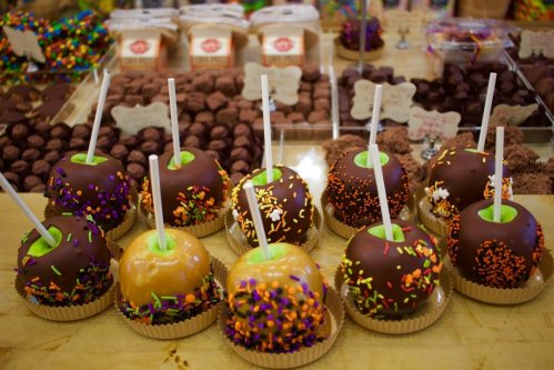 A display of chocolate-covered caramel apples with colorful sprinkles on a table filled with various candies.
