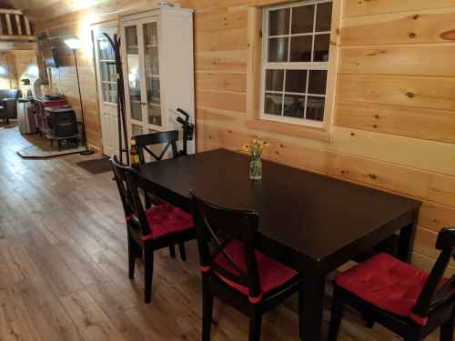 A cozy wooden interior featuring a black dining table with red cushions and a vase of flowers, illuminated softly.
