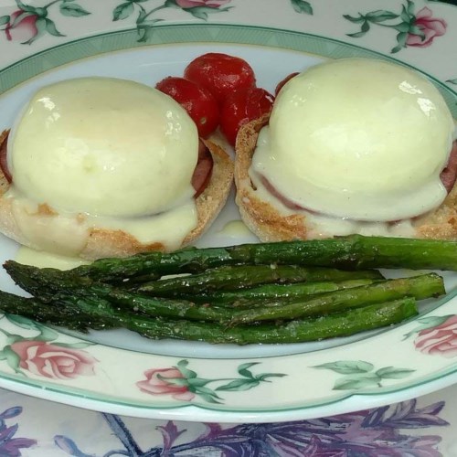 Two eggs Benedict on English muffins with ham, topped with hollandaise sauce, served with asparagus and cherry tomatoes.