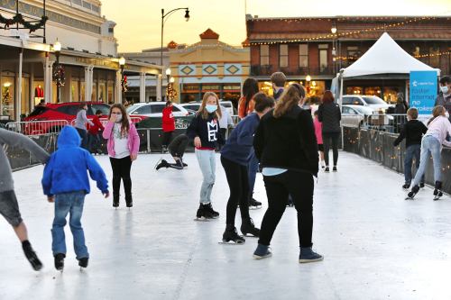 A group of people, including children, ice skating outdoors at a festive venue during sunset.