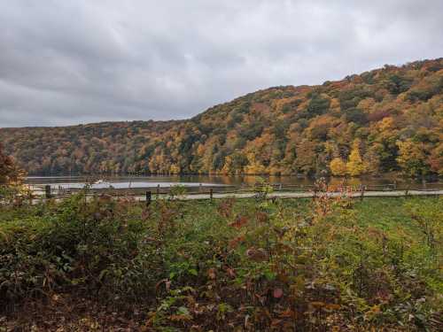 A serene lake surrounded by autumn foliage and rolling hills under a cloudy sky.