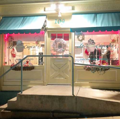 A charming cupcake shop with a yellow exterior, blue awnings, and festive decorations in the windows.