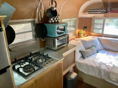 Cozy interior of a camper with a kitchen area, bed, and natural light from windows.