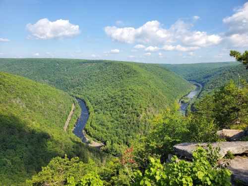 A scenic view of a winding river surrounded by lush green hills under a blue sky with fluffy clouds.