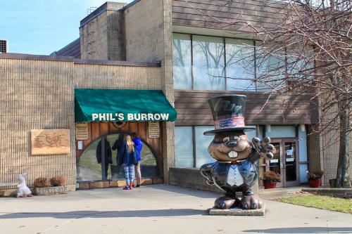 A person enters "Phil's Burrow," featuring a large groundhog statue in a top hat outside the building.