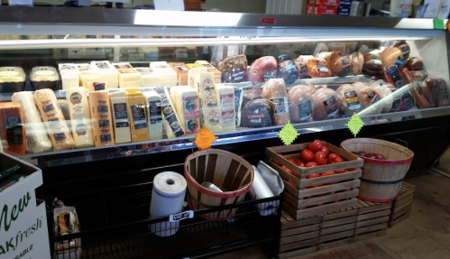 A display case filled with various cheeses and meats, alongside baskets of tomatoes and other items.