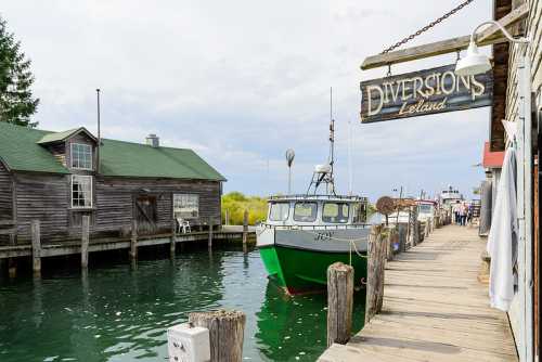 A green boat docked by a wooden pier, with a rustic building and sign for "Diversions" in Leland.