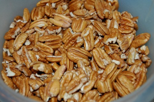 A close-up of a container filled with shelled pecans, showcasing their rich brown color and textured surface.