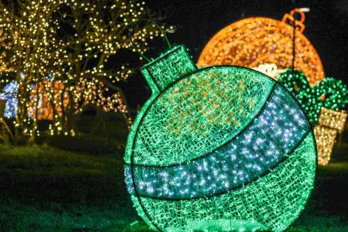 A large green decorative ornament made of lights, surrounded by other illuminated holiday decorations at night.